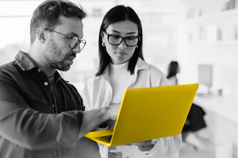 Image of two people looking at a yellow laptop