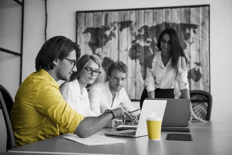 Three coworkers looking at a laptop in a room with a world map on the wall
