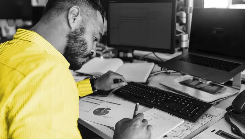 Man writing in a notebook next to computer