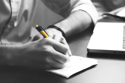 A man writing in a note pad with a yellow pen