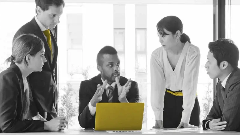 Team meeting around a yellow laptop