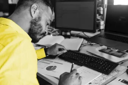 Man writing in a notebook next to computer