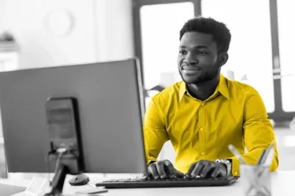 A man in a yellow shirt typing on a computer