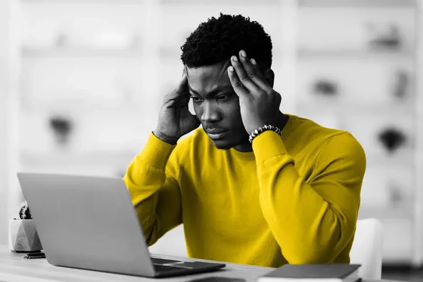 Man holding temples while looking at laptop
