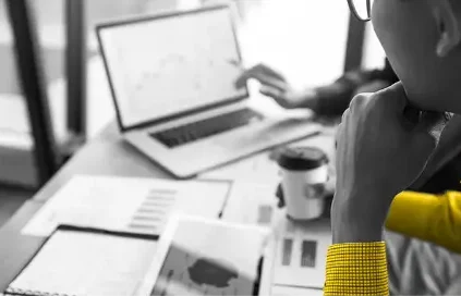 Person in a yellow shirt holding a cup of coffee and looking at a laptop